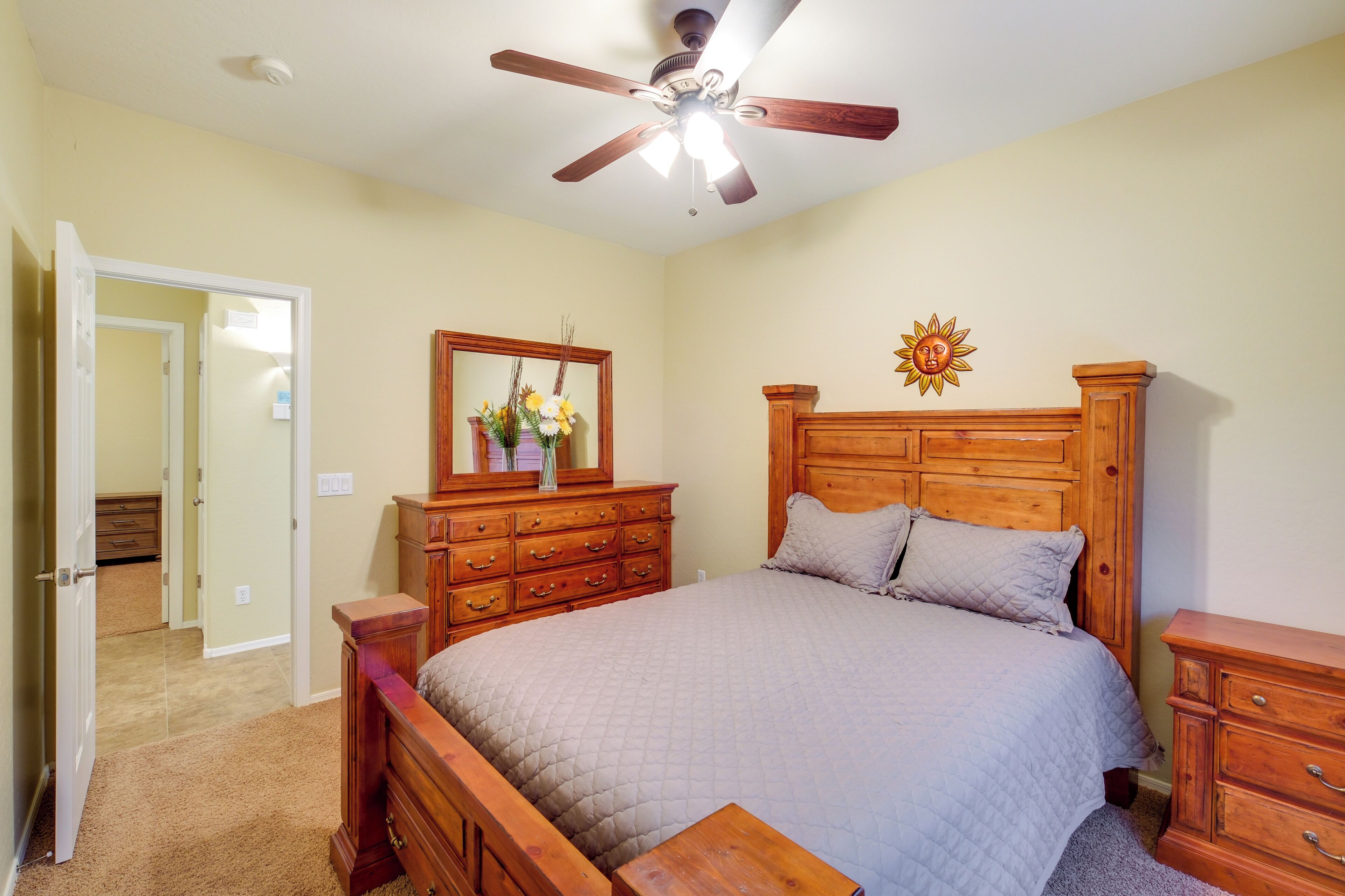 A bedroom with a wooden bed, a ceiling fan, a dresser, and a mirror.