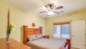 A bedroom with a wooden bed, a ceiling fan, a window with blinds, and a wooden nightstand. - San Tan Valley Home w/ Patio in Johnson Ranch! (San Tan Valley)