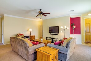 A living room with a ceiling fan, a flat-screen TV, a coffee table, and two sofas.