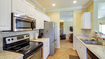 A kitchen with white cabinets, stainless steel appliances, granite countertops, and a brown carpet.