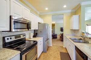 Una cocina con gabinetes blancos, electrodomésticos de acero inoxidable, encimeras de granito y alfombra marrón.