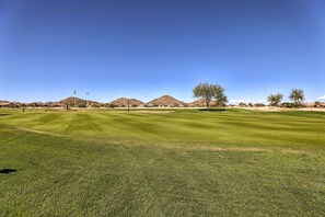 Un campo de golf bien cuidado con cielos despejados, montañas a lo lejos y pocos árboles.