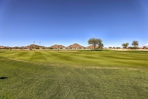 Un campo de golf bien cuidado con cielos despejados, montañas a lo lejos y pocos árboles.