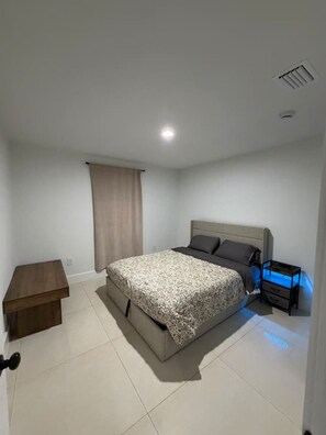 A bedroom with a bed, bedside table, and a nightstand with a blue light. - Modern Miami Home near Wynwood, Downtown & S Beach (Miami)