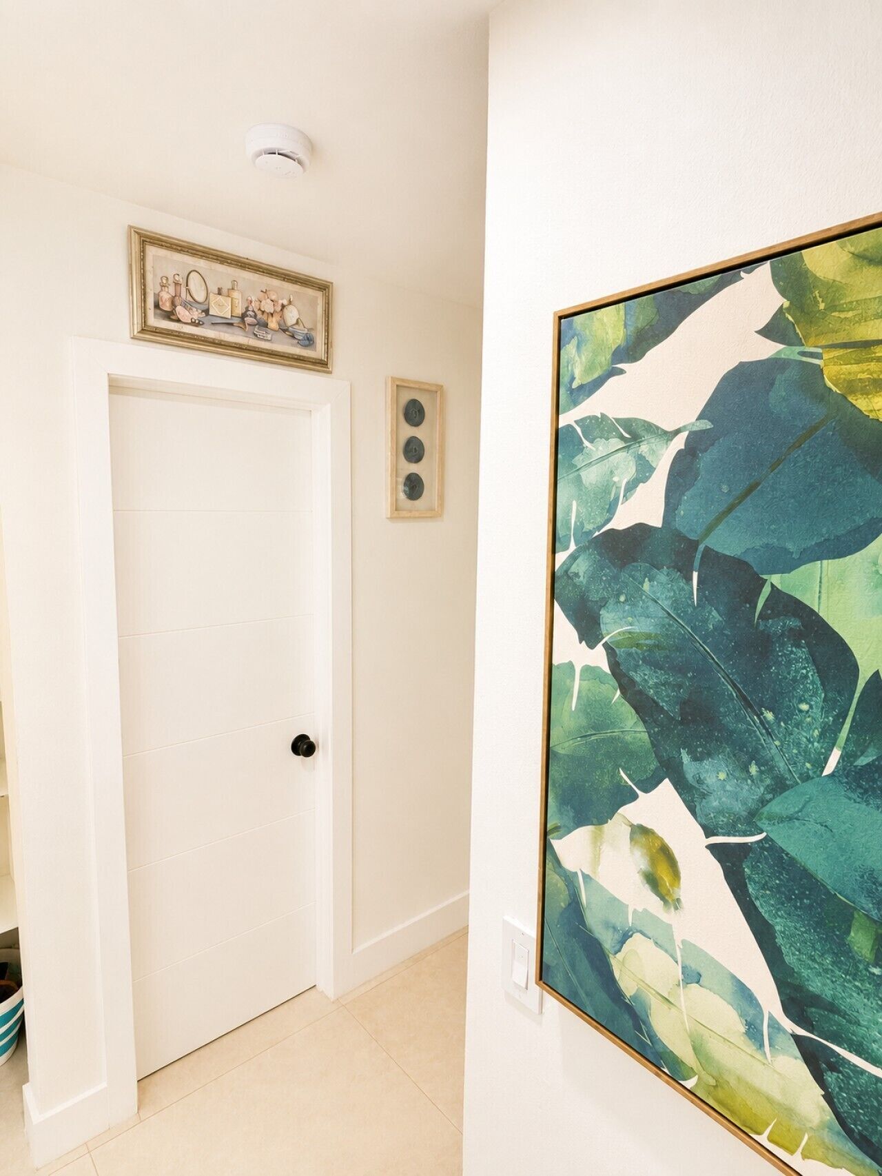 A hallway with a white door, a framed picture above it, and a large abstract painting on the wall.