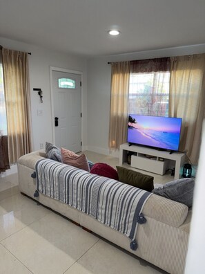 A living room with a sofa, TV, and curtains. - Modern Miami Home near Wynwood, Downtown & S Beach (Miami)