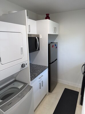 A compact kitchen with a washer-dryer unit, a microwave, and a refrigerator. - Modern Miami Home near Wynwood, Downtown & S Beach (Miami)