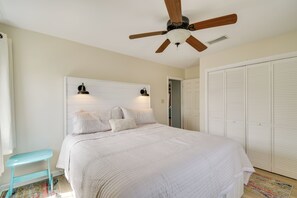 Ein Schlafzimmer mit Bett, Deckenventilator, Nachttisch, Fenster und Kleiderschrank.