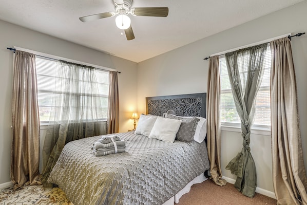 A bedroom with a bed, curtains, a ceiling fan, and a nightstand with a lamp.