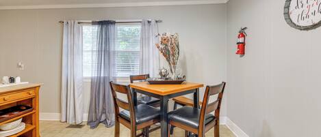 A dining area with a wooden table, four chairs, a window with curtains, a fire extinguisher, and a wall-mounted sign.