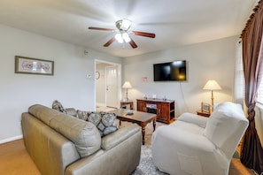 Una sala de estar con ventilador de techo, televisor, sofá, sillón, mesa de centro y lámpara.