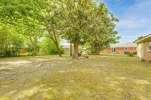 A grassy backyard with trees, a brick building, and a wooden fence.