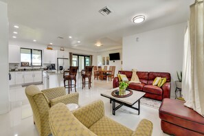 Ein modernes Wohnzimmer mit einem roten Sofa, gelben Stuhlen mit Muster und einem Couchtisch. Im Hintergrund ist eine Küche zu sehen.