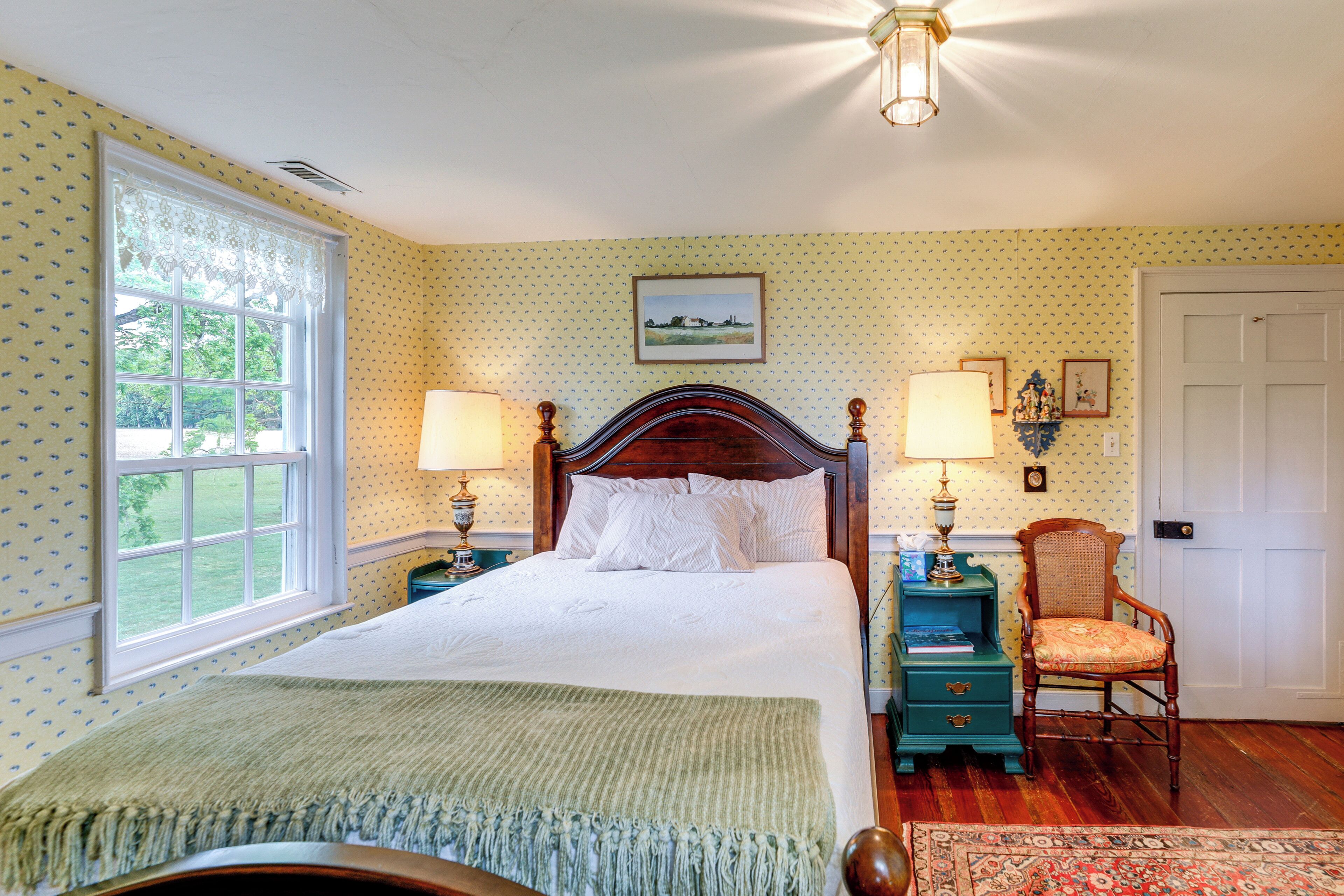 A bedroom with a large bed, two bedside tables, a chair, a window, and a door.