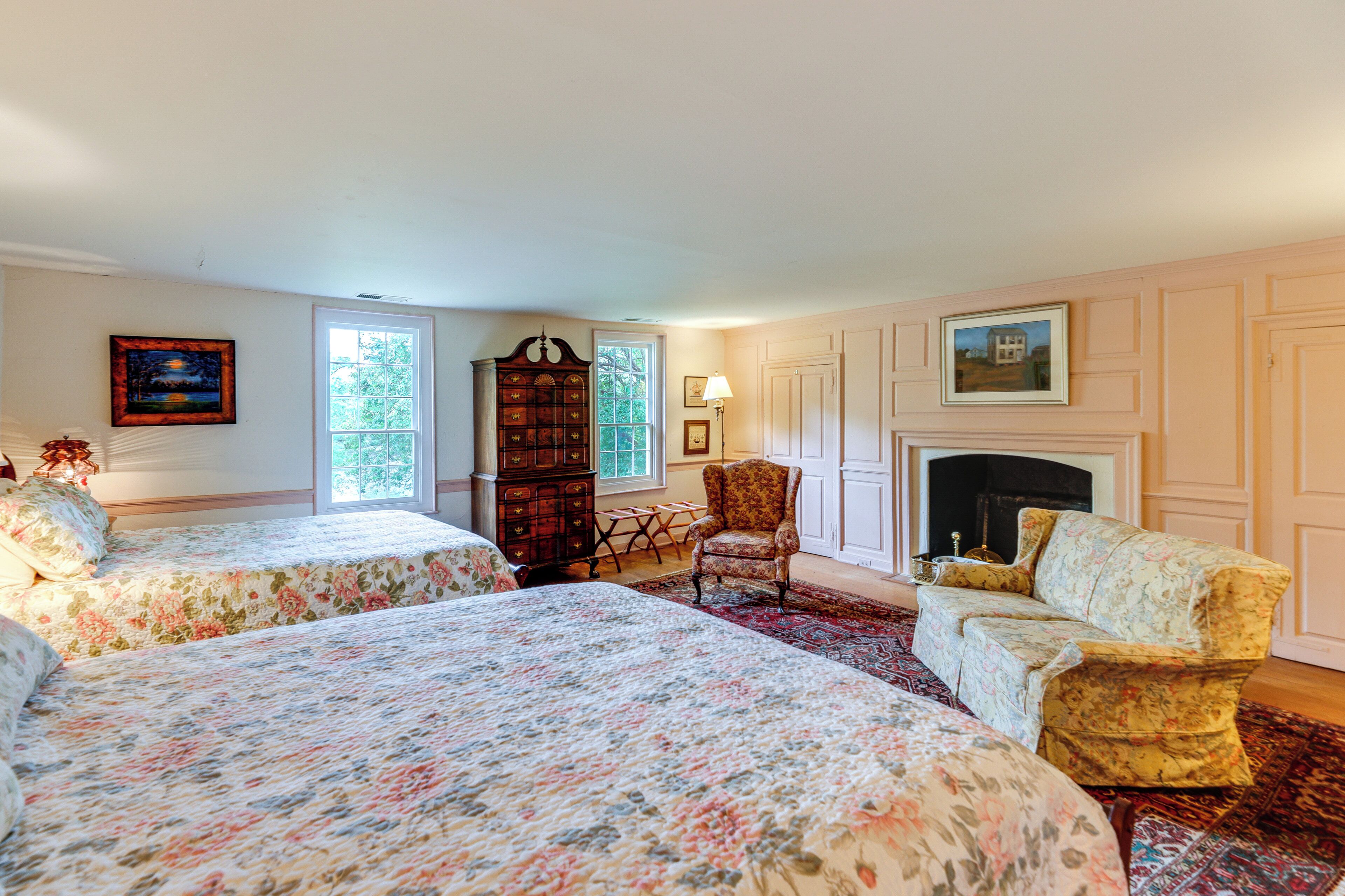 A bedroom with two beds, a fireplace, a wooden cabinet, and a chair.