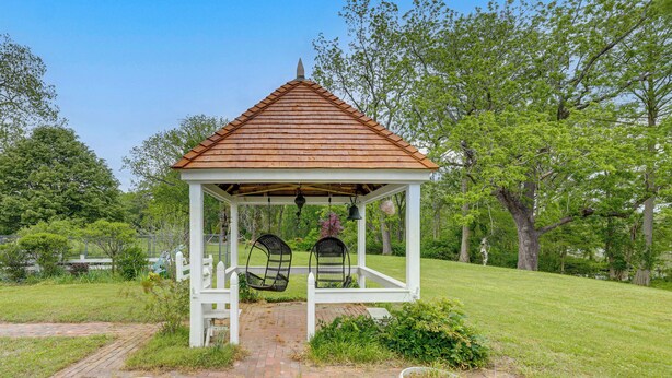 A gazebo with a tiled roof, two swings, and a brick pathway leading to it.