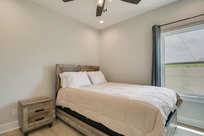 Une chambre à coucher avec un lit, une table de chevet, un ventilateur de plafond et une fenêtre.