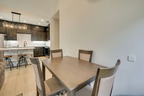A modern kitchen with dark cabinetry, a central island, and a dining area with a wooden table and chairs.