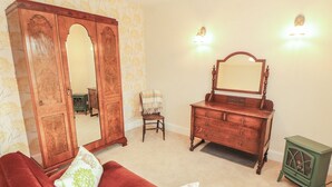 A room with a red sofa, a wooden dresser with a mirror, a green cabinet, and a chair. - East View (Kirkby Stephen)