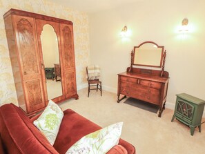 Ein Zimmer mit einem roten Sofa, einem Holzkleiderschrank mit Spiegel, einem grünen Schrank und einem Sessel.