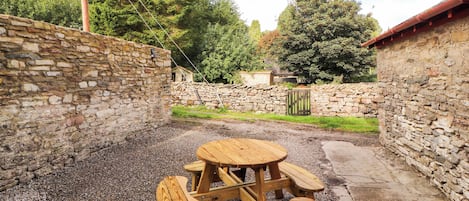 A stone wall, a wooden table with benches, and a gravel ground.