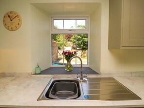 A kitchen with a built-in sink, a clock on the wall, and a window overlooking a garden. - East View (Kirkby Stephen)