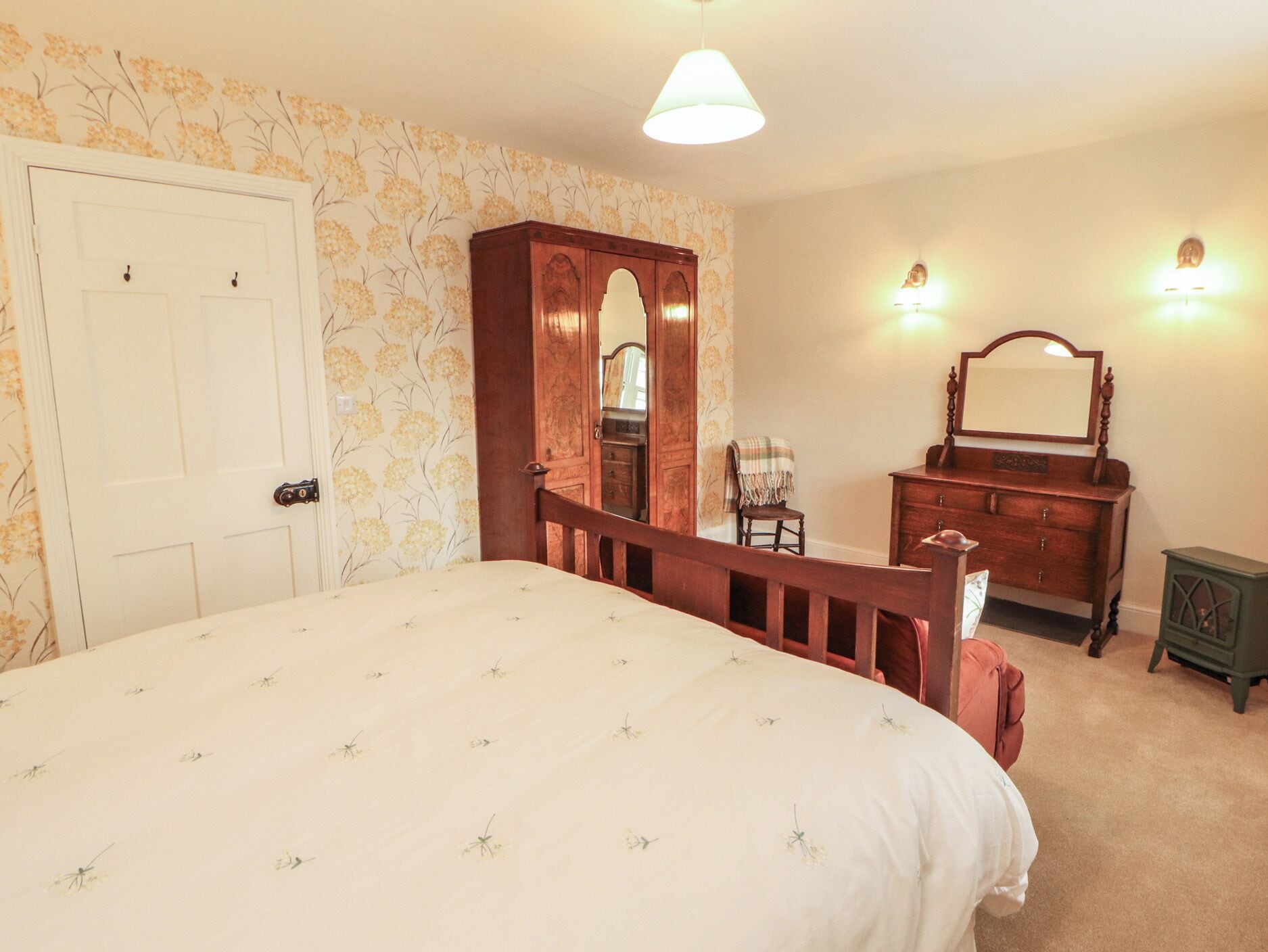 Une chambre à coucher comprenant un lit, une armoire en bois, une chaise, une commode et un petit meuble.
