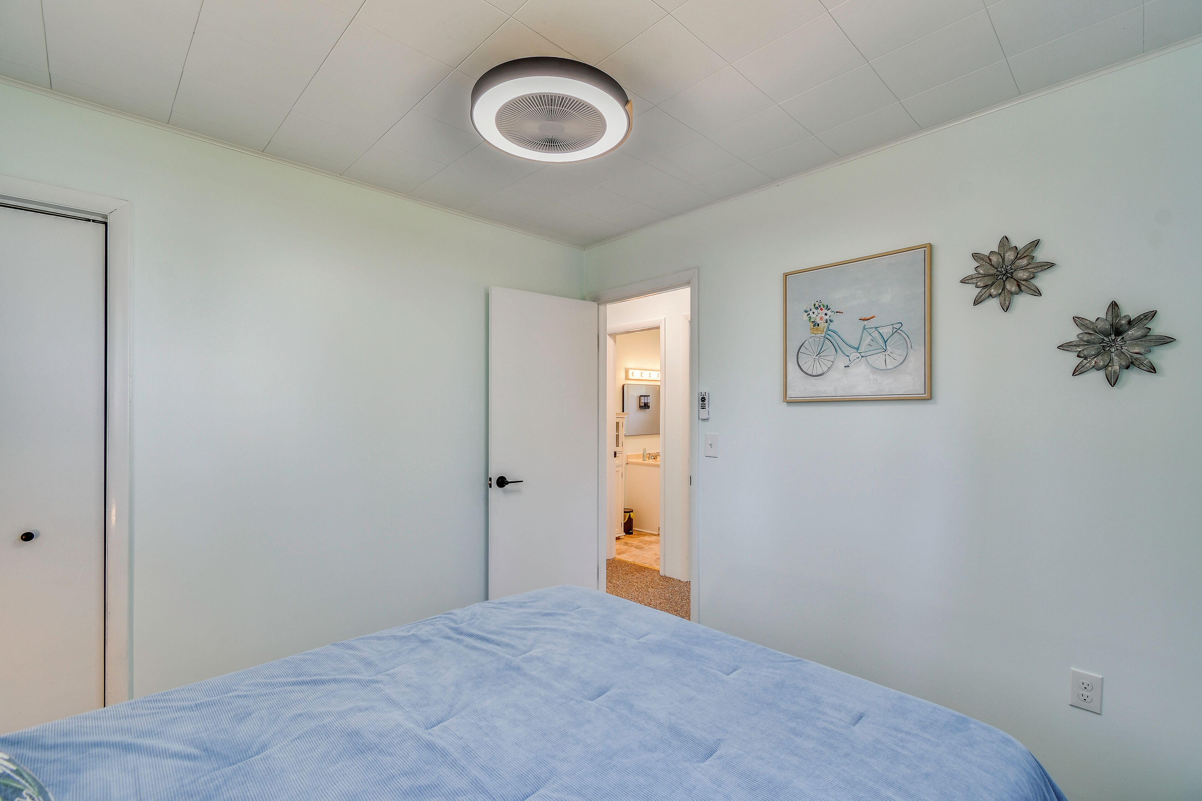 A bedroom with a bed, a door, a ceiling fan, and a hallway leading to a bathroom.