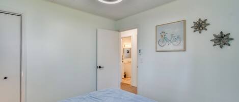 A bedroom with a bed, a door, a ceiling fan, and a hallway leading to a bathroom.