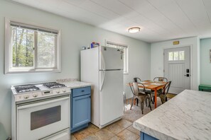 Eine Küche mit Herd, Backofen, Kühlschrank und Esstisch mit Stühlen.