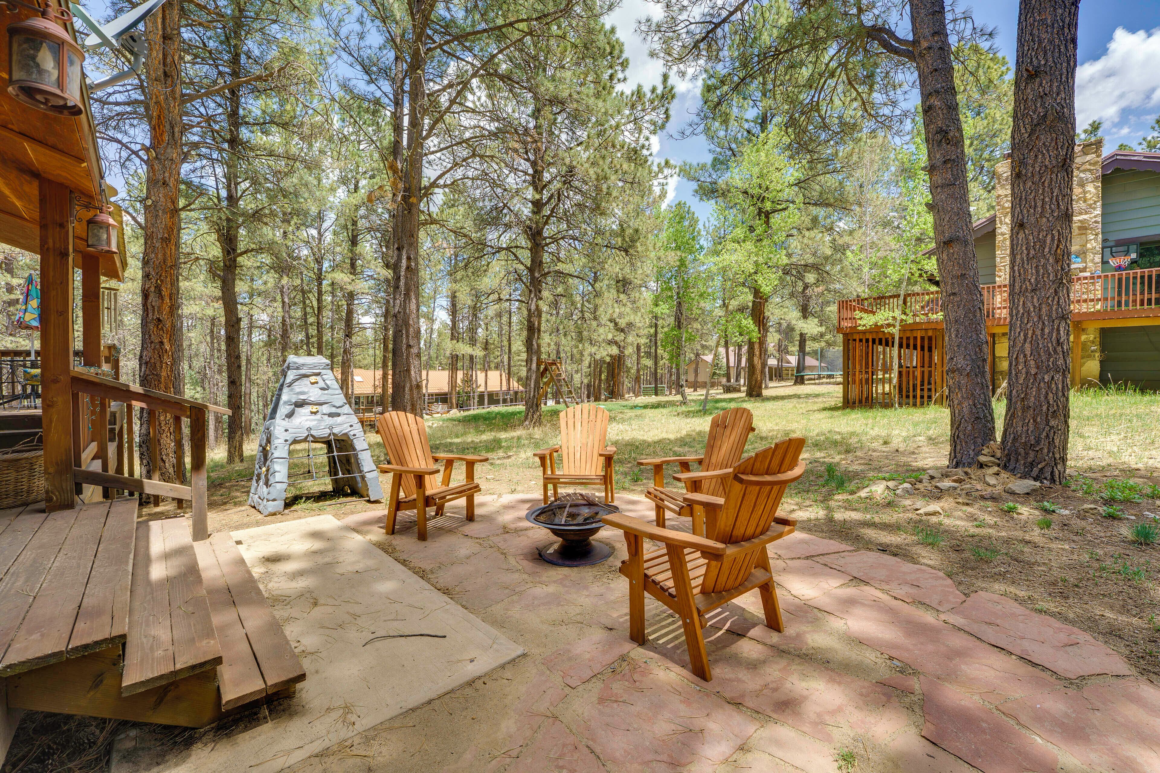 A wooden deck with Adirondack chairs and a fire pit, surrounded by trees.