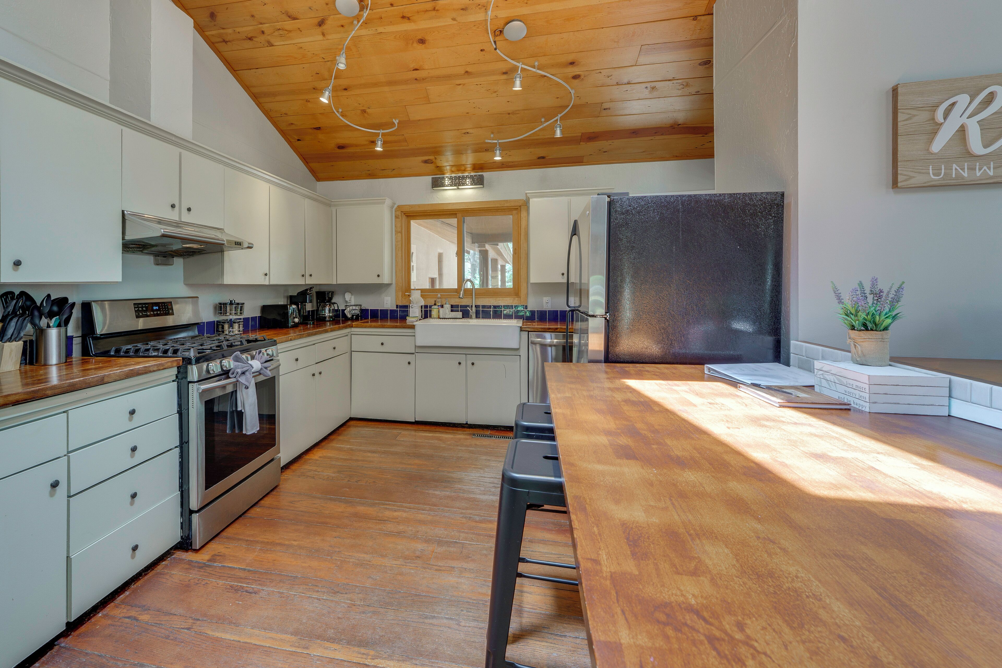A modern kitchen with wooden ceiling, stainless steel appliances, and a long wooden table.