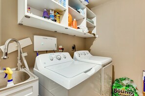 A laundry area with two washing machines, a sink, and a shelf with various cleaning supplies. - Harps Lake Family Retreat on 3 Private Acres (Ellenwood)
