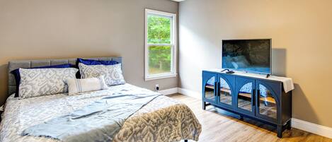 A bedroom with a bed, a window, a ceiling fan, and a TV on a stand.