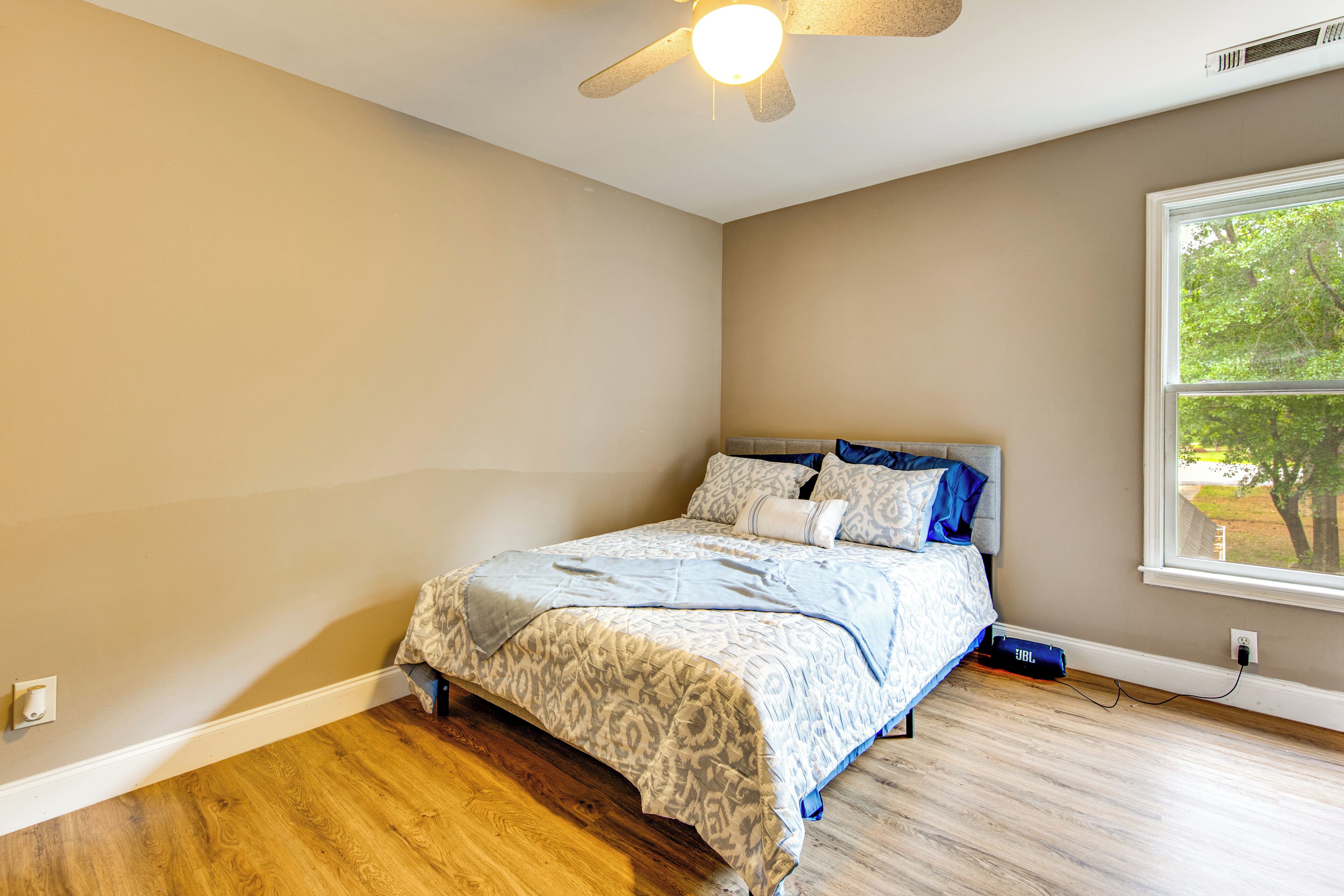 Un dormitorio con cama, ventilador de techo, ventana con vistas y suelo de madera.