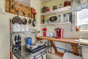 Uma cozinha com fogão, panelas, frigideiras, torradeira e micro-ondas.