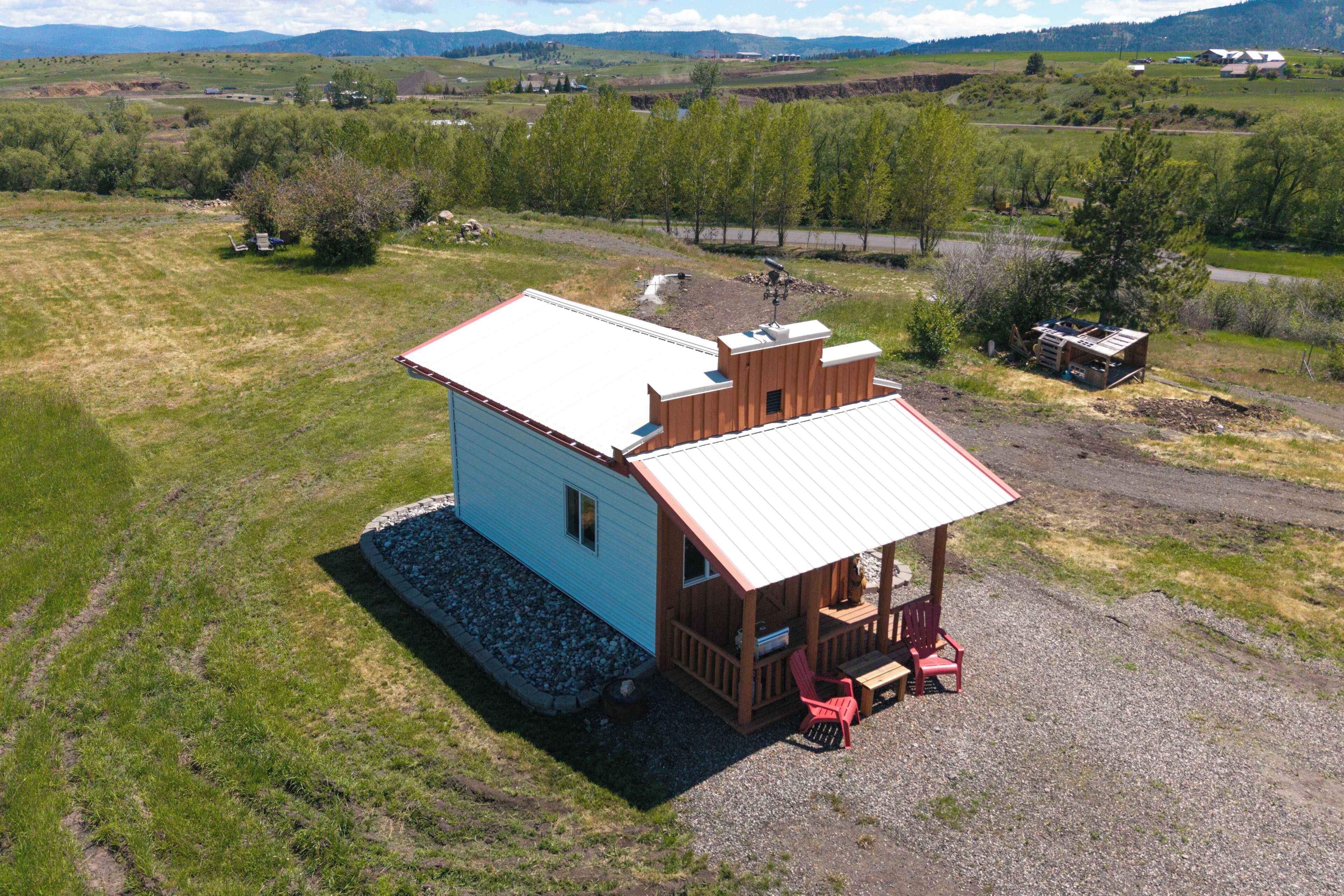 A small cabin with a porch, a small shed, and a gravel driveway.