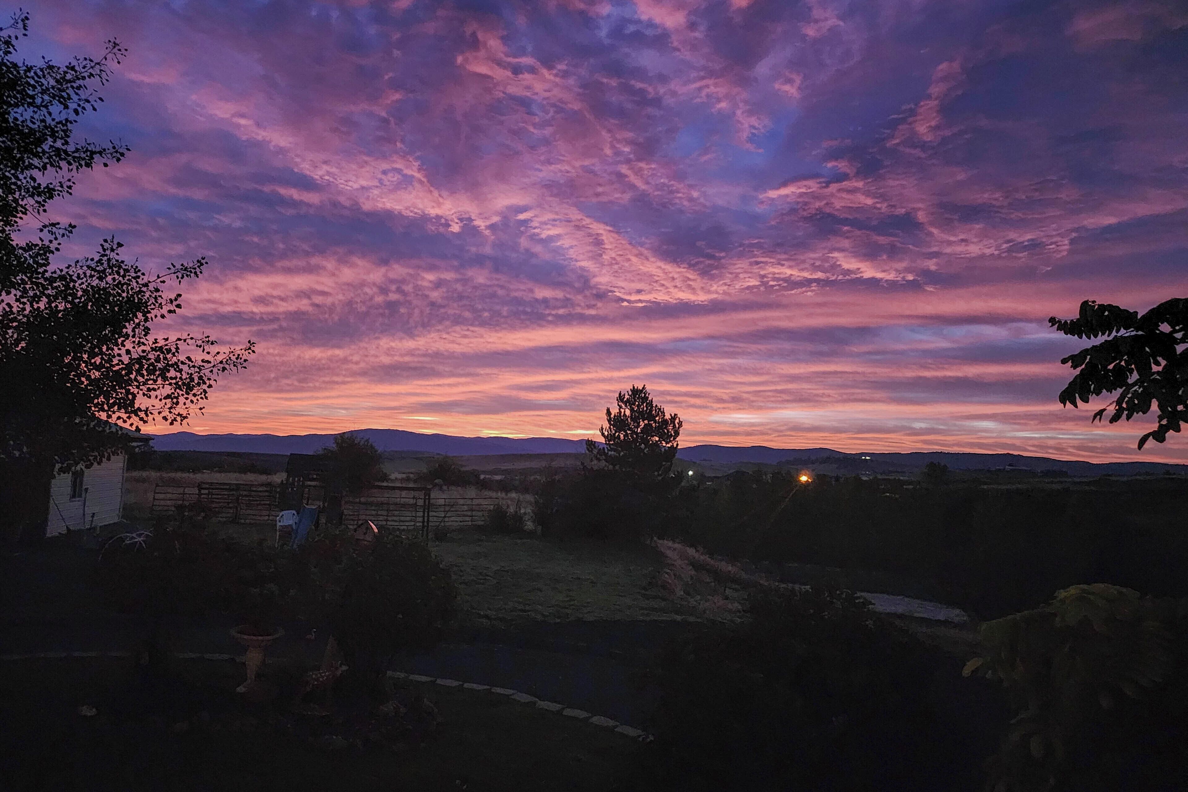 Un paisaje rural con cielo al atardecer, una cerca y un edificio pequeño.