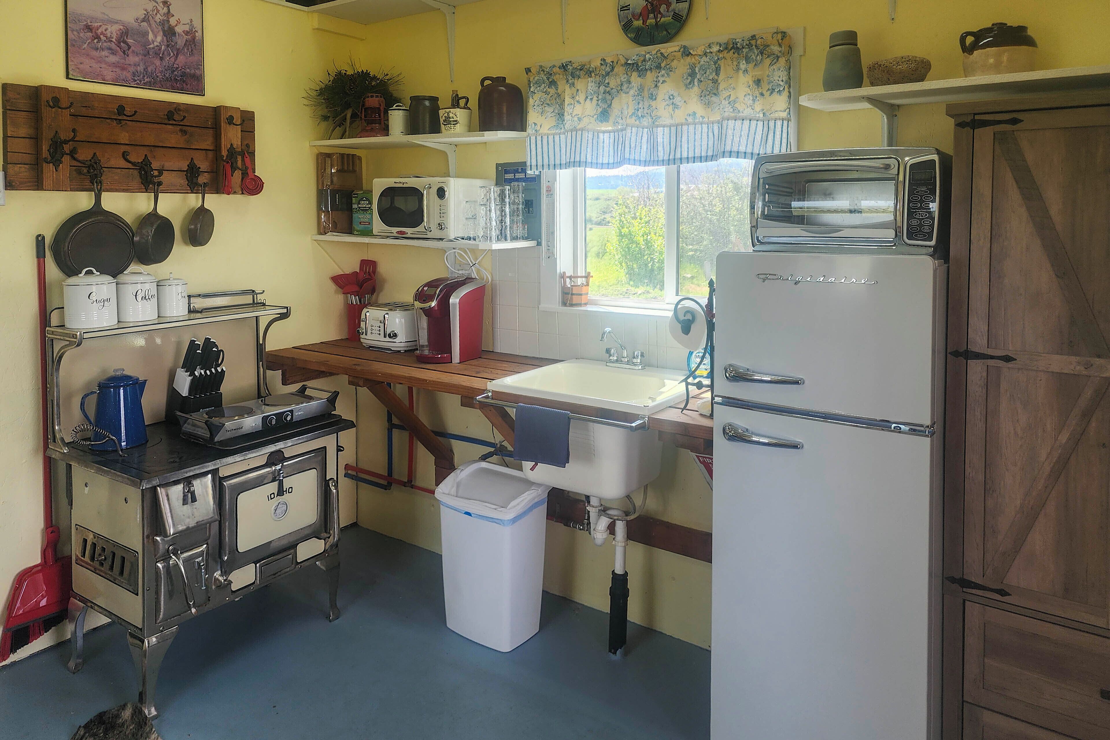 Una cocina con estufa, microondas, tostadora, fregadero y alacenas.