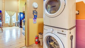 Een wasruimte met een wasmachine en droger, een brandblusser, een bord met informatie en een klein krukje.