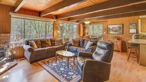 A cozy cabin interior with a fireplace, wooden walls, large windows, a dining area, and a kitchen. - Cozy Cabin on the Cove, Large Deck & Private Dock (Groveland)
