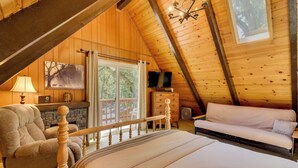 An attic bedroom with a bed, a sofa, a chair, a TV, and a fireplace. - Cozy Cabin on the Cove, Large Deck & Private Dock (Groveland)