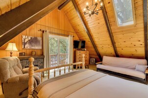 An attic bedroom with a bed, a sofa, a chair, a TV, and a fireplace.