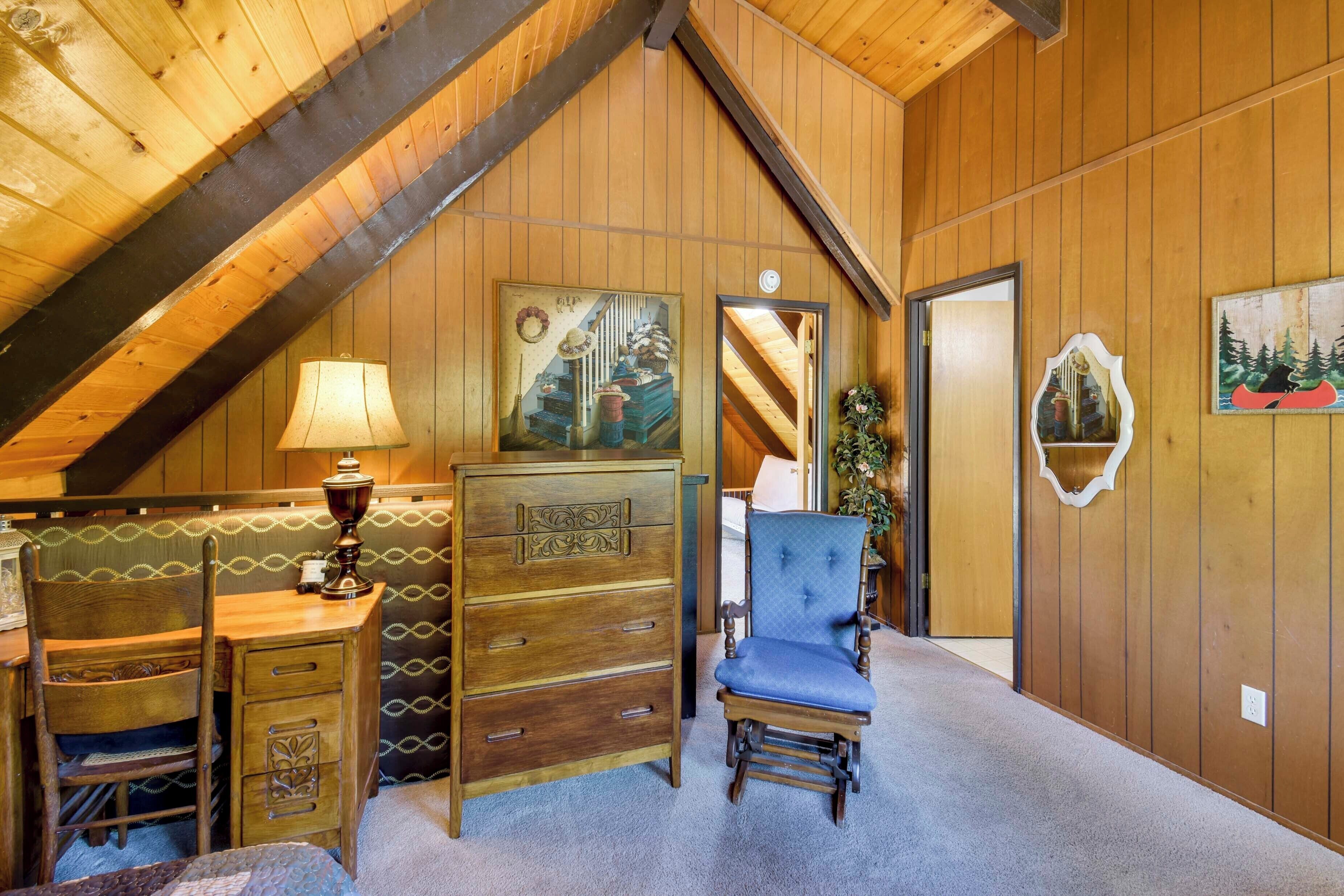 A wooden interior with a high ceiling, a desk with drawers, a chair, and a lamp.
