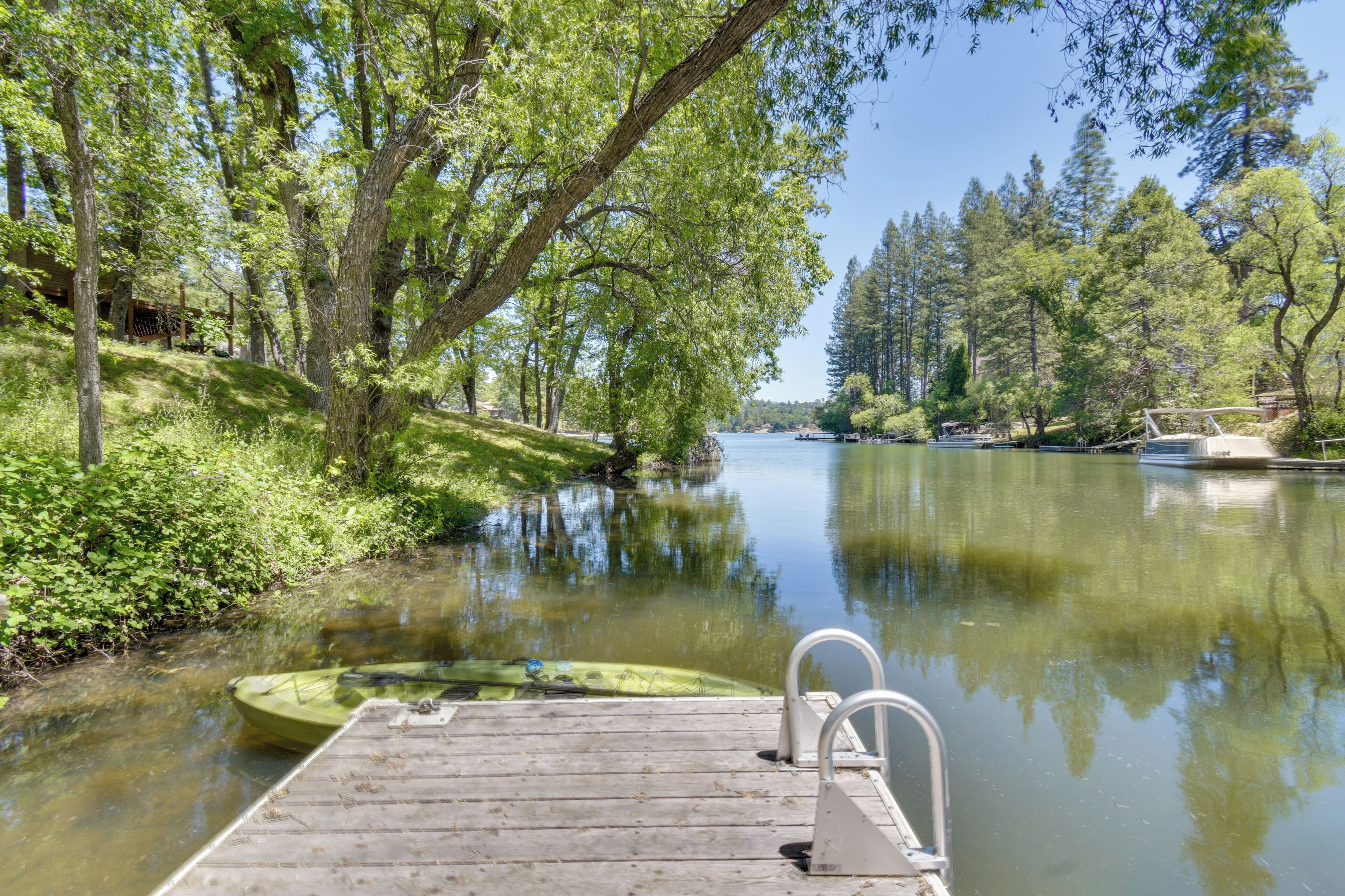 A wooden dock extending into a calm river, surrounded by lush greenery and trees.