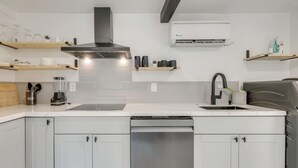 A modern kitchen with white cabinets, a stainless steel dishwasher, a black range hood, and a wall-mounted air conditioner. - Sleek Studio 4 Mi to Dtwn Phoenix: Pets Welcome! (Phoenix)