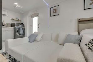 Ein modernes, helles Zimmer mit einer Couch, einer Waschmaschine und einem Bett.