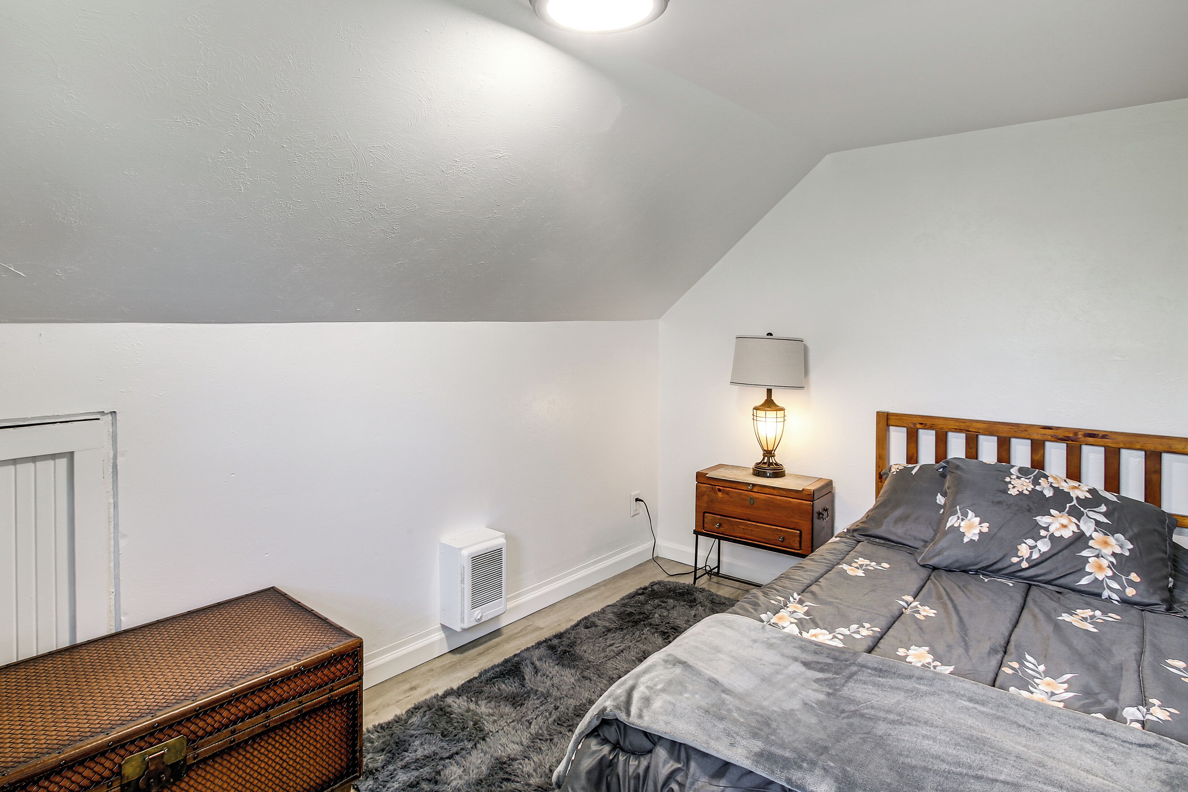 A bedroom with a bed, a nightstand, a lamp, a radiator, and a suitcase.