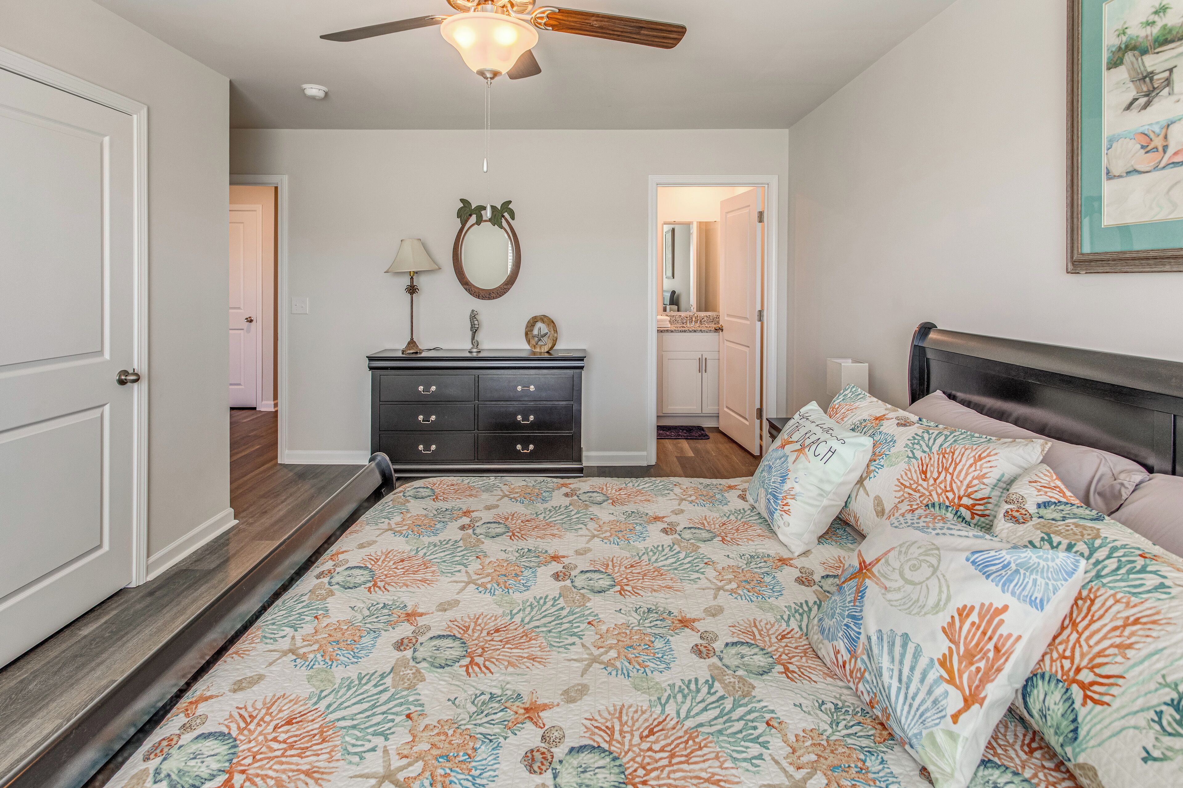 A bedroom with a bed, dresser, ceiling fan, and a door leading to another room.