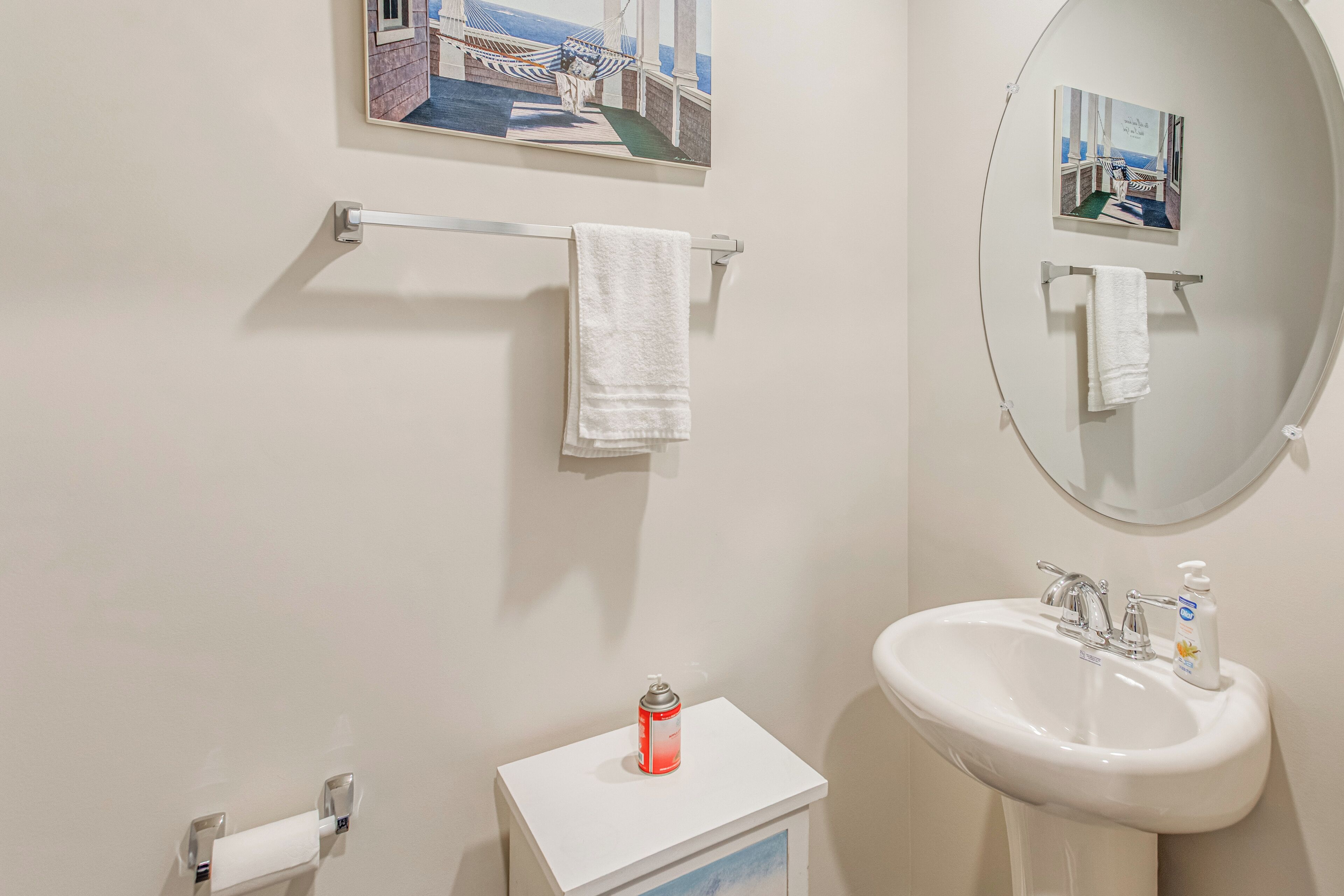 A bathroom with a white sink, a mirror, a towel rack, a toilet paper holder, and a small shelf with a red can.
